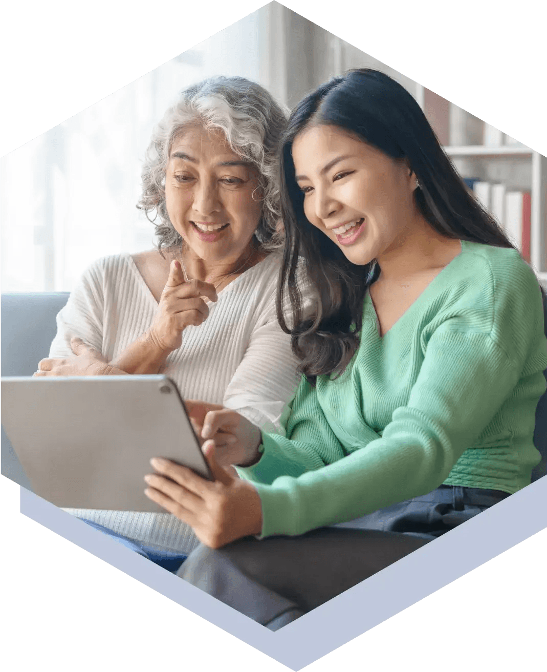 A daughter holding a tablet and smiling, showing her grandmother something on the screen.