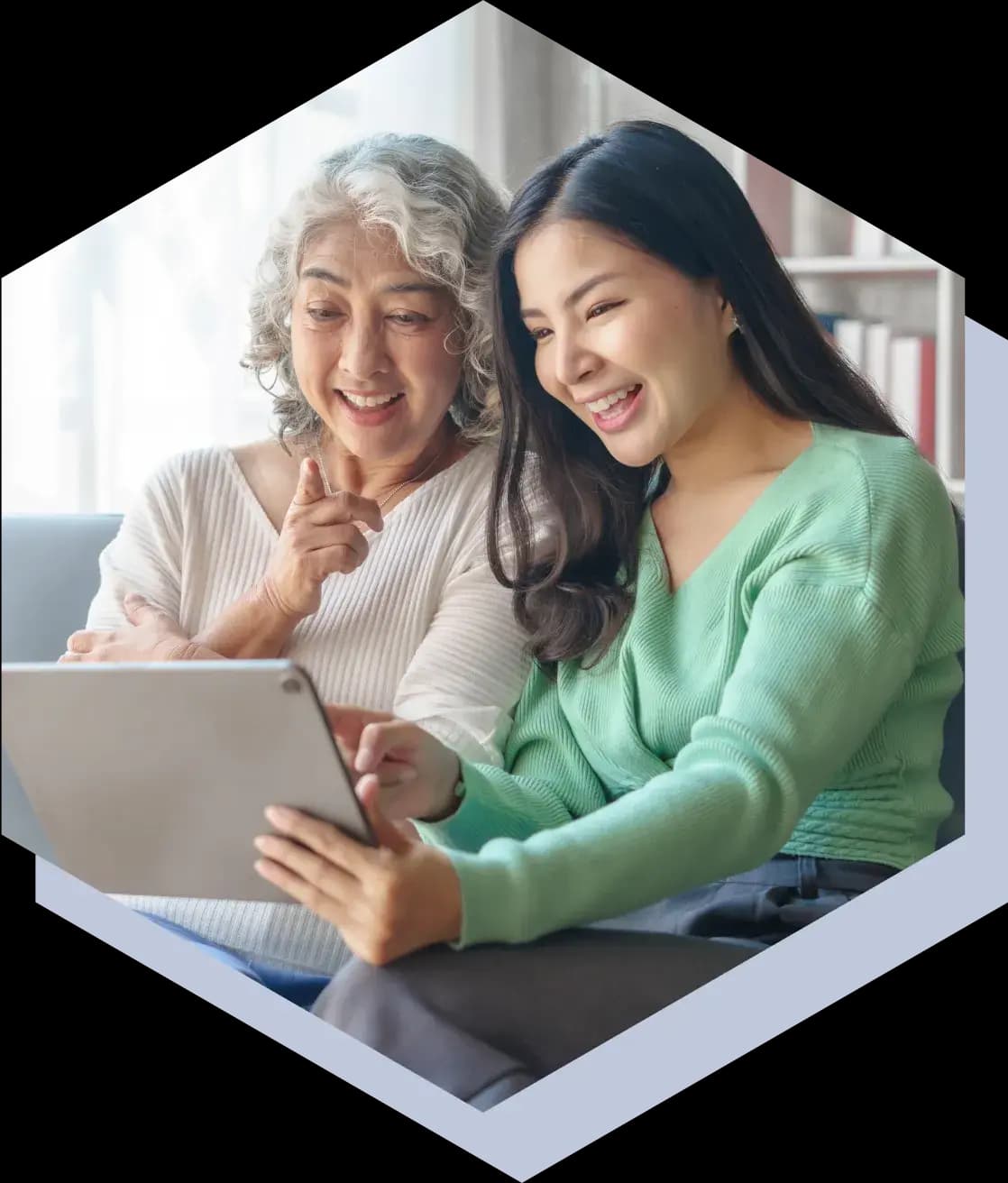 A young woman holding a tablet and smiling, showing her grandmother something on the screen.